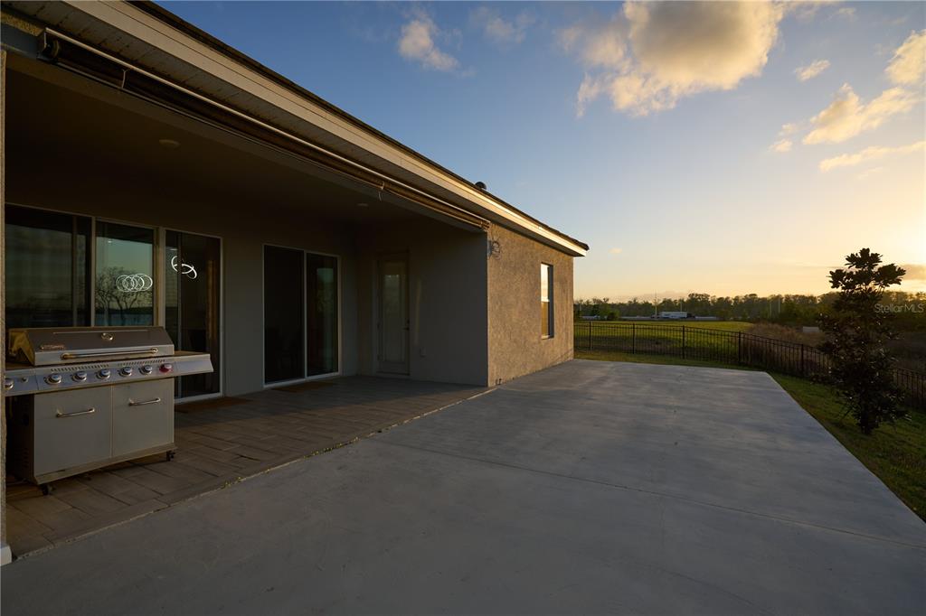 A covered concrete patio features a stainless steel grill and a view of a backyard — 17854 HITHER HILLS CIRCLE, WINTER GARDEN, FL