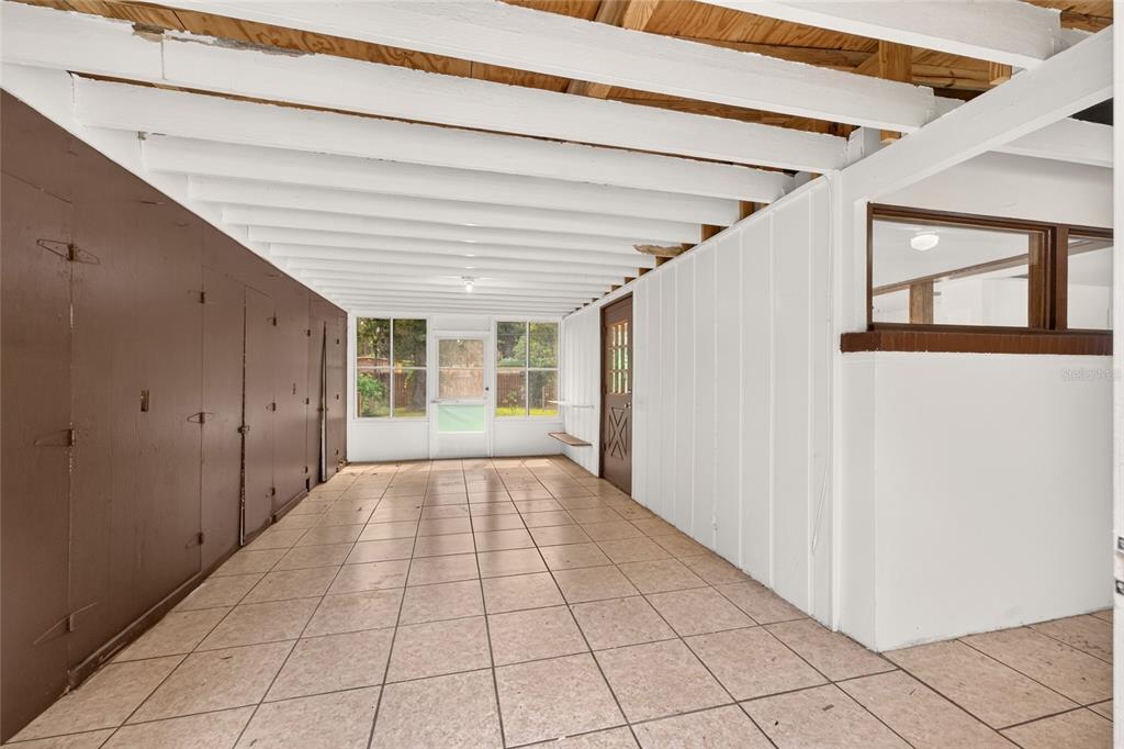 A covered patio with tiled flooring, white exposed beams, and a brown paneled wall — 2125 NE 6TH TERRACE, GAINESVILLE, FL