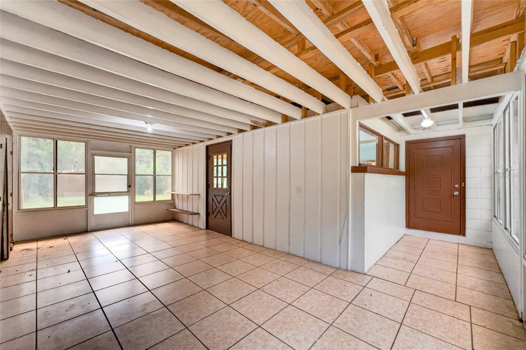 A sunroom with tiled floors, exposed ceiling beams, and two brown doors — 2125 NE 6TH TERRACE, GAINESVILLE, FL