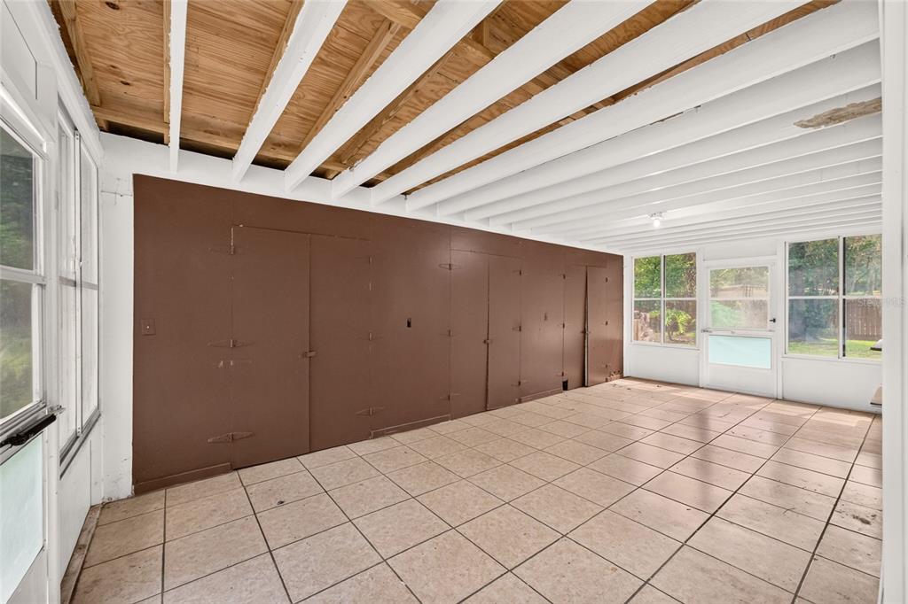 An enclosed porch with a tiled floor, exposed ceiling beams, and a brown paneled wall — 2125 NE 6TH TERRACE, GAINESVILLE, FL