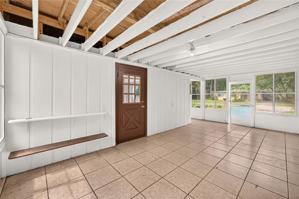 A sunroom with white paneled walls, exposed ceiling joists, tiled flooring, and a brown door — 2125 NE 6TH TERRACE, GAINESVILLE, FL
