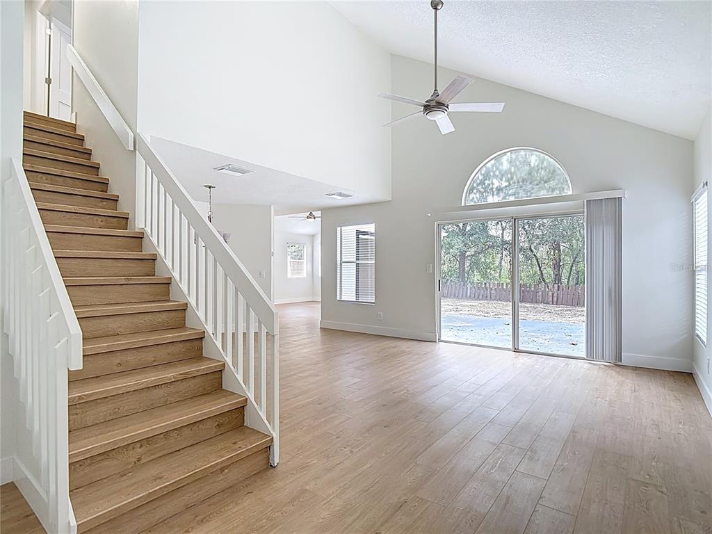 A living room with wood-look flooring, a staircase, vaulted ceilings, and sliding glass doors — 2013 GLEN FORGE STREET, BRANDON, FL