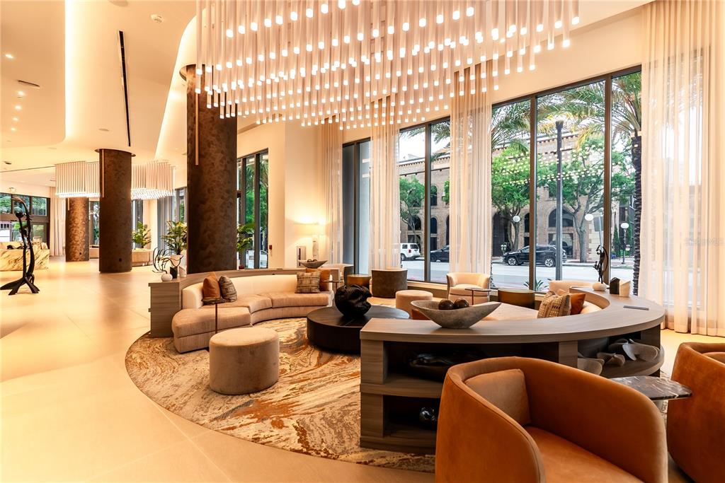 A modern hotel lobby features curved seating, a large chandelier, and floor-to-ceiling windows — 275 1ST AVENUE S UNIT 1504, ST PETERSBURG, FL