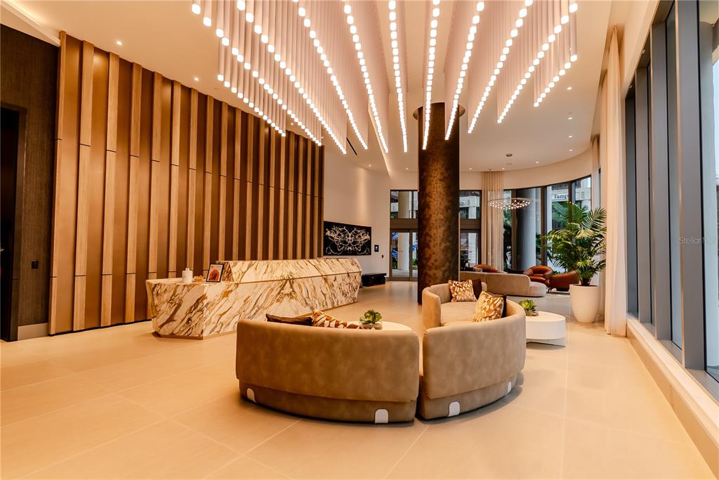 A modern lobby features a marble reception desk, curved seating, and hanging pendant lights — 275 1ST AVENUE S UNIT 1504, ST PETERSBURG, FL