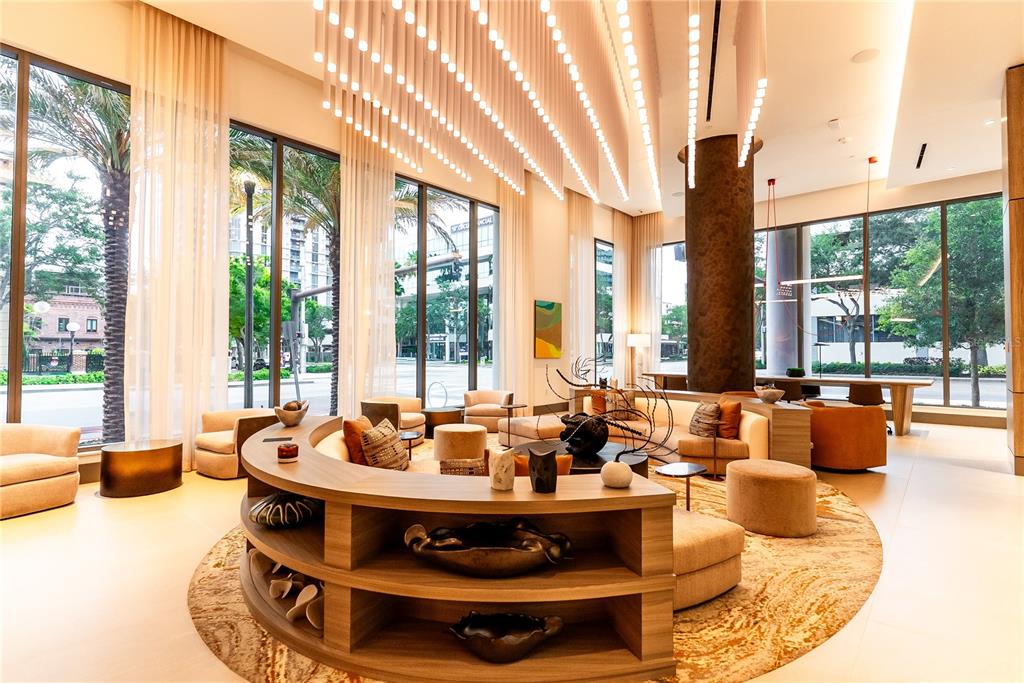 A modern lobby features a curved wooden bookshelf, plush seating, and hanging linear light fixtures — 275 1ST AVENUE S UNIT 1504, ST PETERSBURG, FL