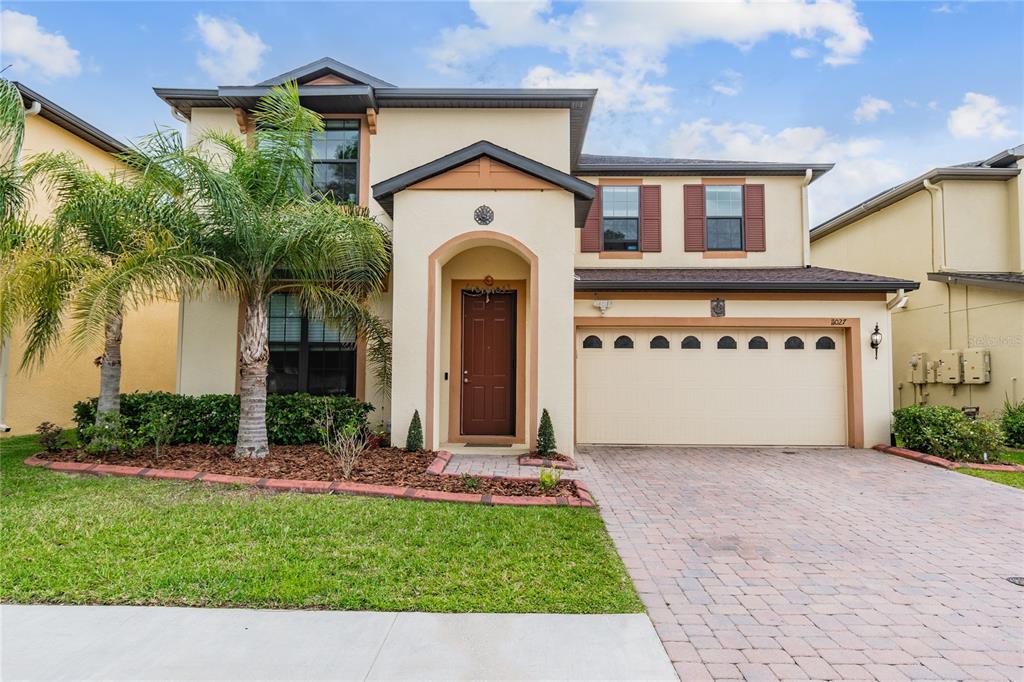 A two-story suburban house with a tan stucco exterior, a palm tree, and a garage — 11027 TAHITI ISLE LANE, TAMPA, FL