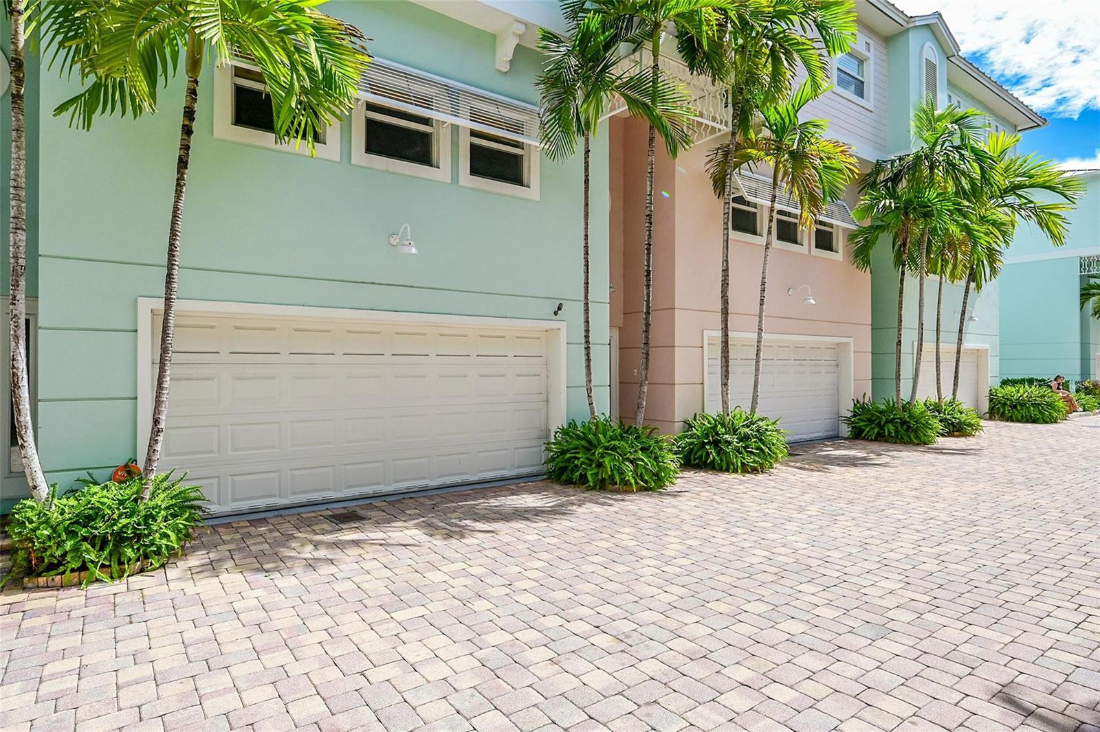 A row of pastel-colored townhouses with attached garages and palm trees on a paved driveway — 453 NE 1st Street, Pompano Beach FL 33060, POMPANO BEACH, FL