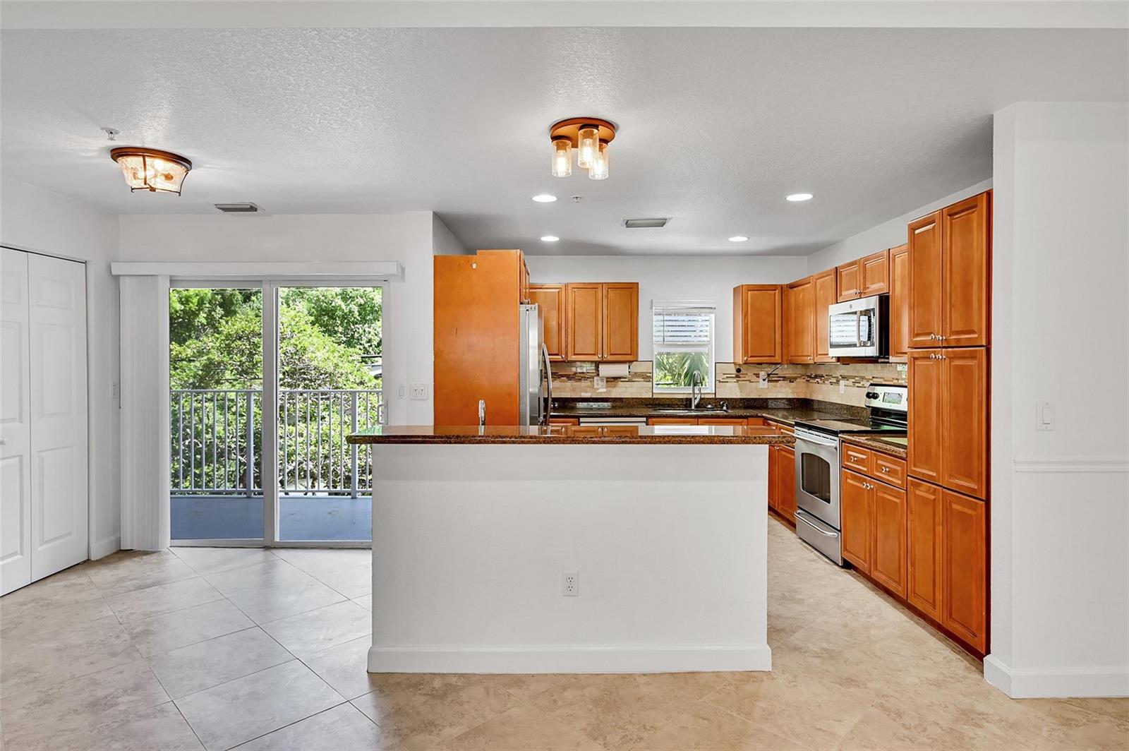 A kitchen with wood cabinets, granite countertops, and a breakfast bar overlooks a balcony — 453 NE 1st Street, Pompano Beach FL 33060, POMPANO BEACH, FL