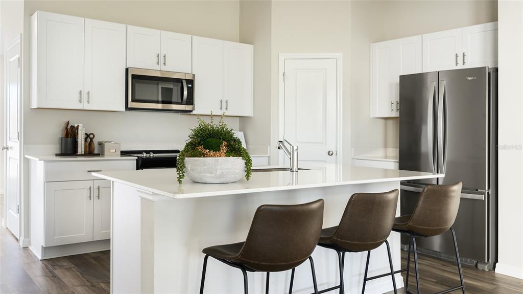 A modern kitchen features white cabinets, stainless steel appliances, a center island, and bar stools — 33607 NOBLE CREEK PLACE, DADE CITY, FL