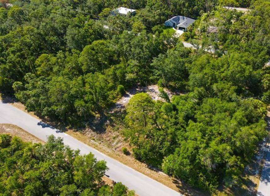 An aerial view shows a vacant, wooded residential lot situated along a paved road — 13406 DOUBLEDAY AVENUE, PORT CHARLOTTE, FL
