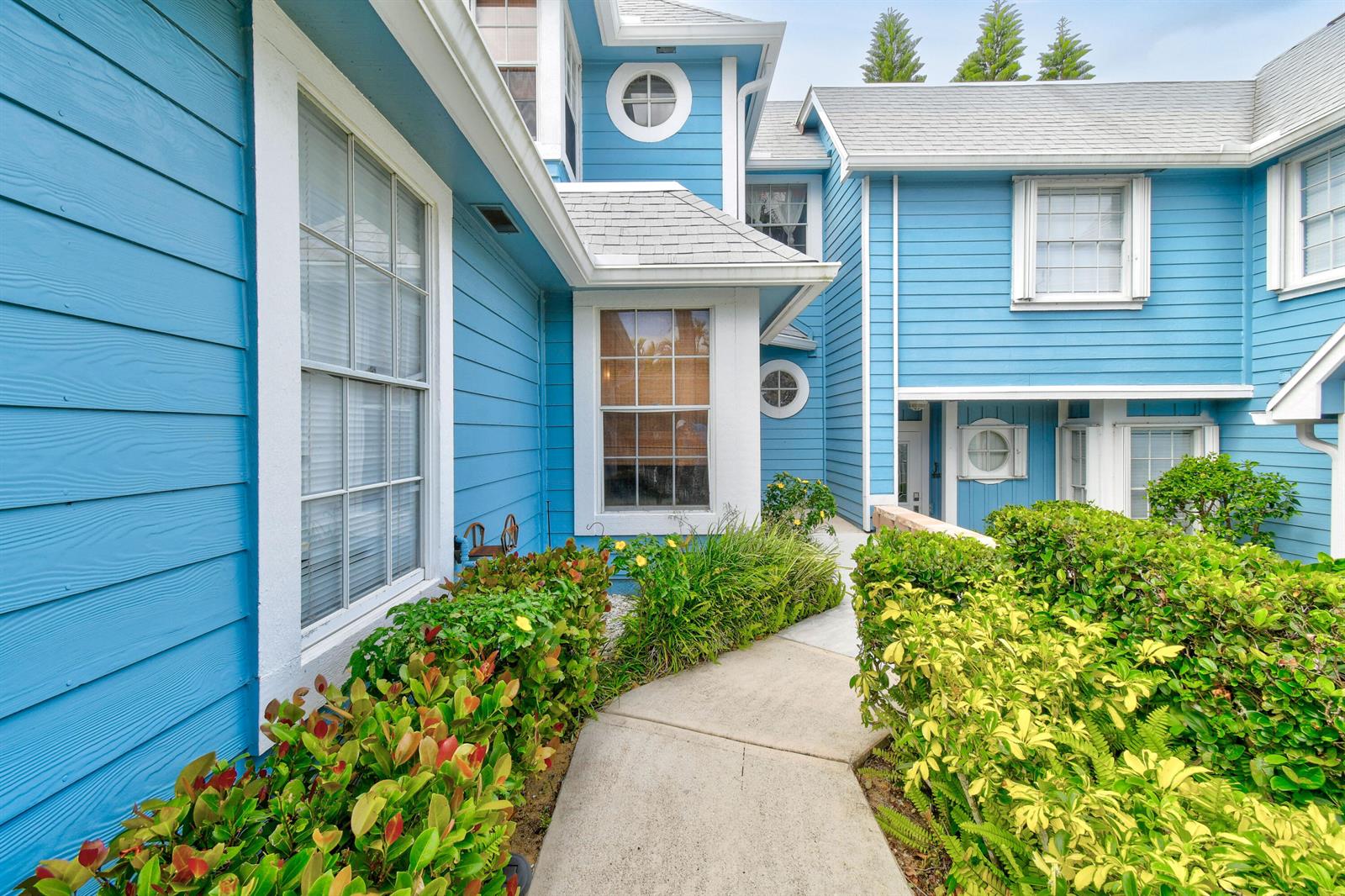 A concrete walkway leads to the entrance of a blue-sided house with white trim — 1003 Ocean Dunes Circle, Jupiter FL 33477, JUPITER, FL