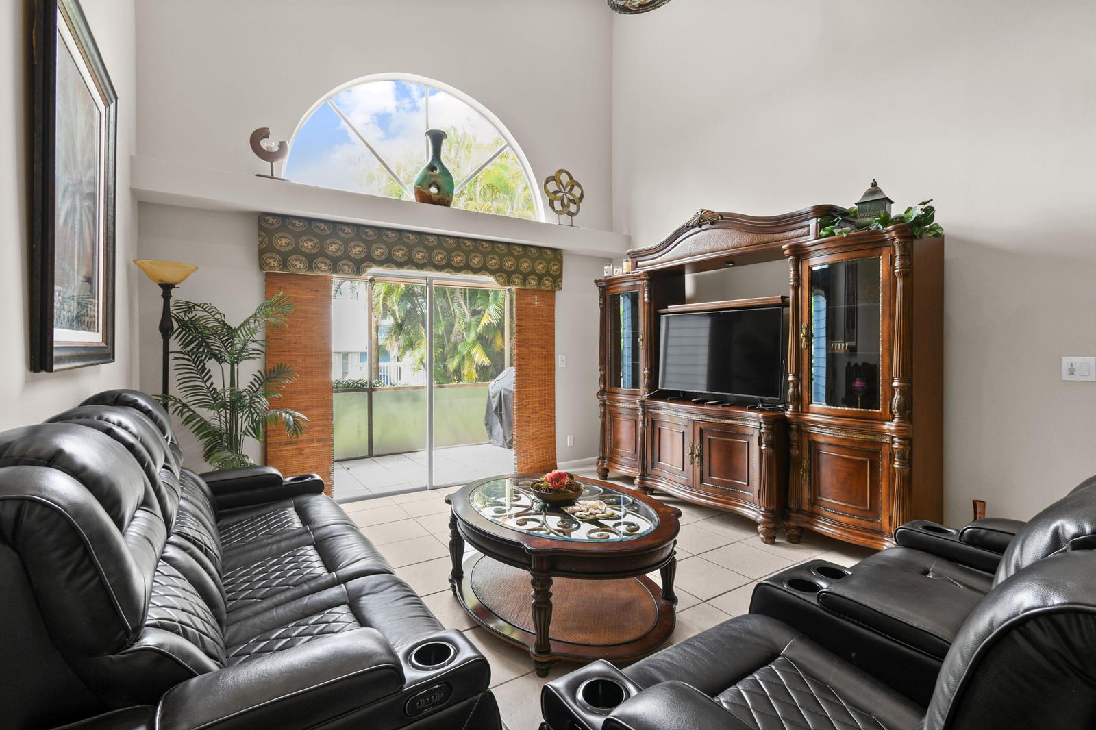 A living room features black leather recliners, a wooden entertainment center, and a large arched window — 1003 Ocean Dunes Circle, Jupiter FL 33477, JUPITER, FL