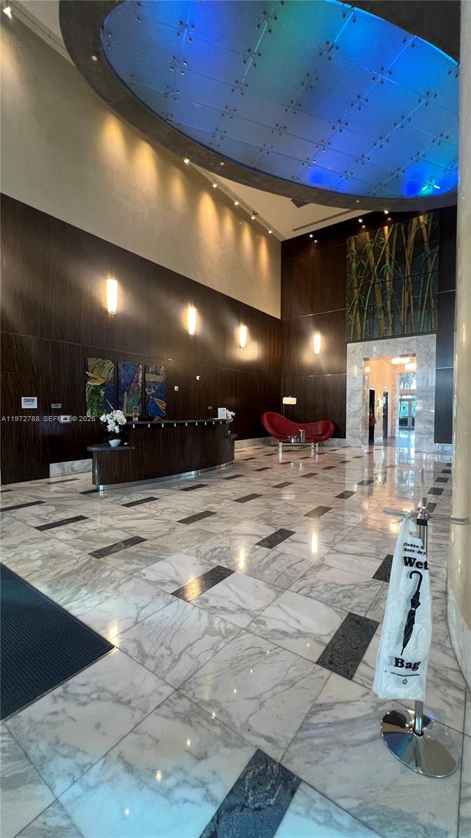A modern building lobby features a curved reception desk, marble flooring, and a red sofa — 185 SW 7th St # 2202, Miami FL 33130, MIAMI, FL
