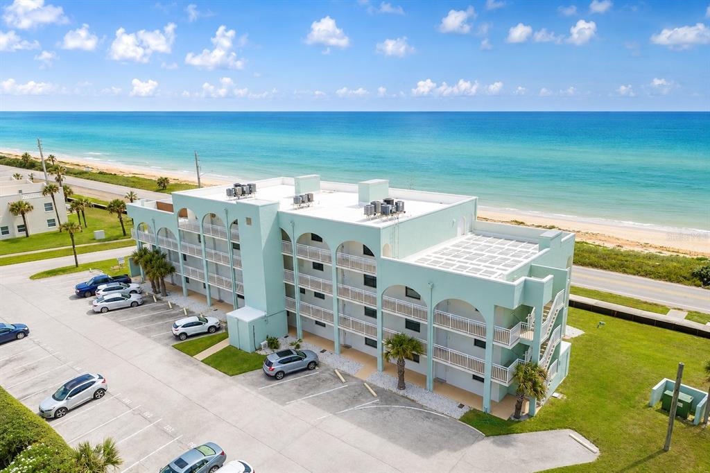 An aerial view of a light green, multi-story oceanfront apartment building with a parking lot — 3390 OCEAN SHORE BOULEVARD UNIT 1050, ORMOND BEACH, FL