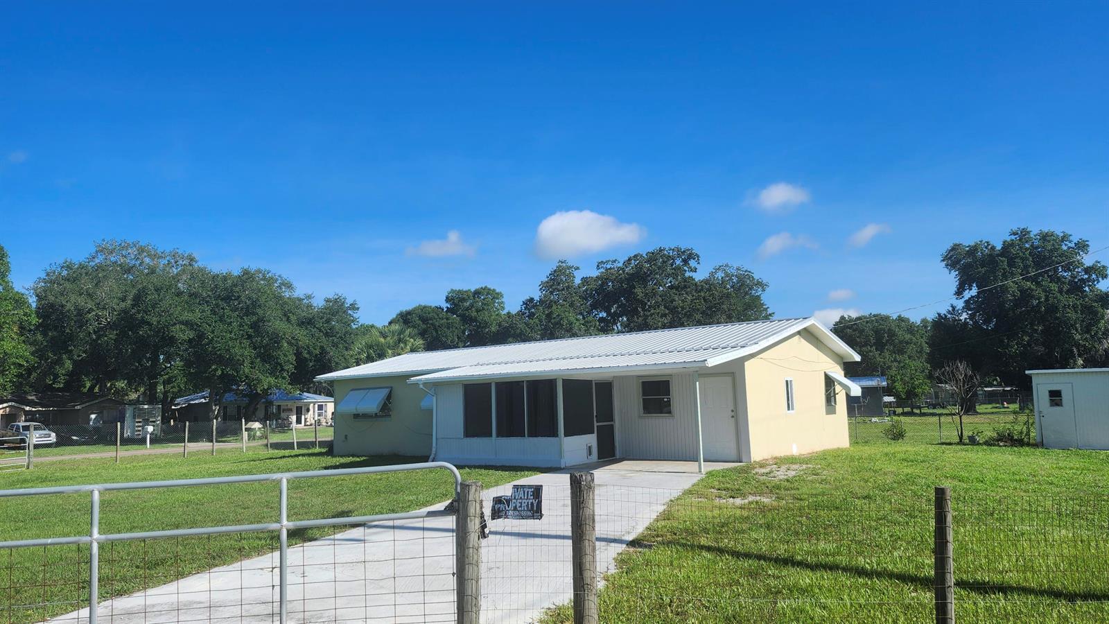 A single-story house with a white metal roof and a screened porch sits on grass — 3751 NW 36th Street, Okeechobee FL 34972, OKEECHOBEE, FL