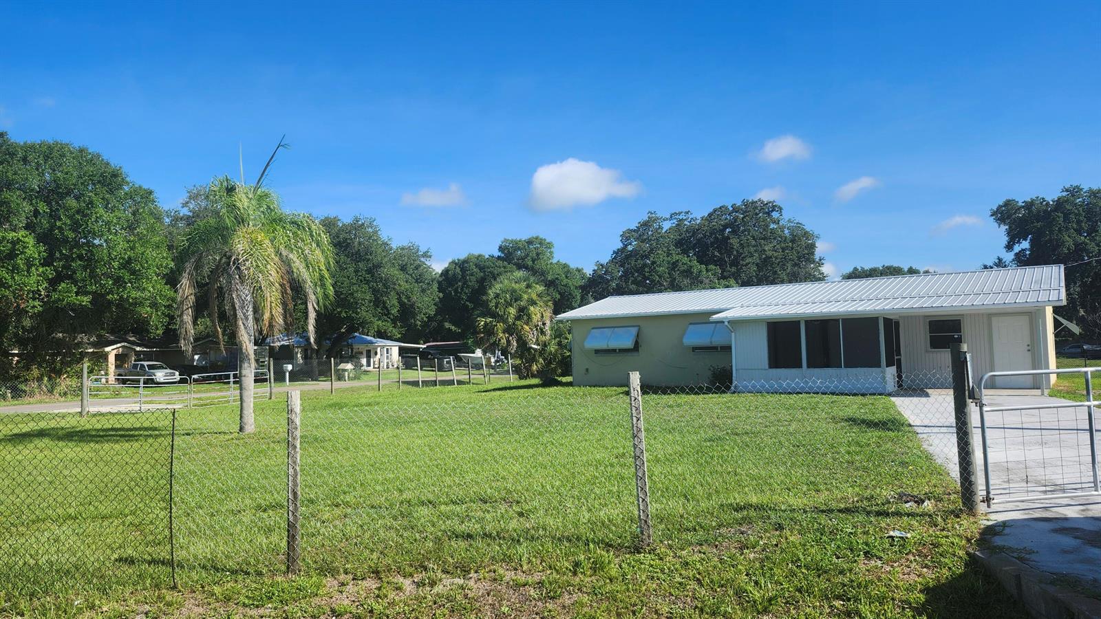 A single-story house with a metal roof and a fenced yard under a blue sky — 3751 NW 36th Street, Okeechobee FL 34972, OKEECHOBEE, FL