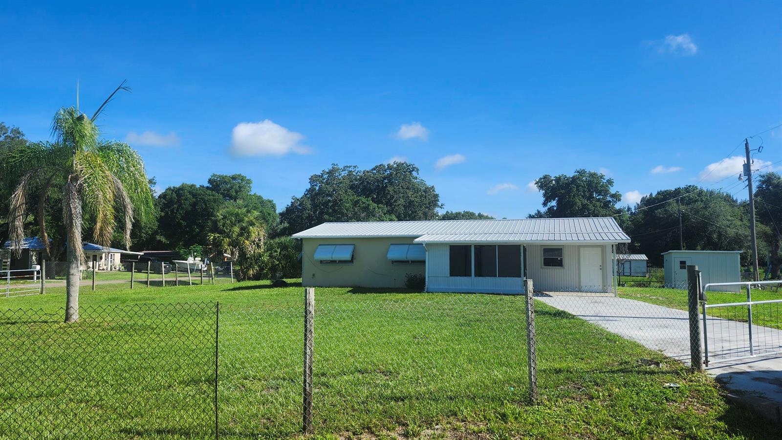 A single-story house with a metal roof and a fenced yard under a blue sky — 3751 NW 36th Street, Okeechobee FL 34972, OKEECHOBEE, FL