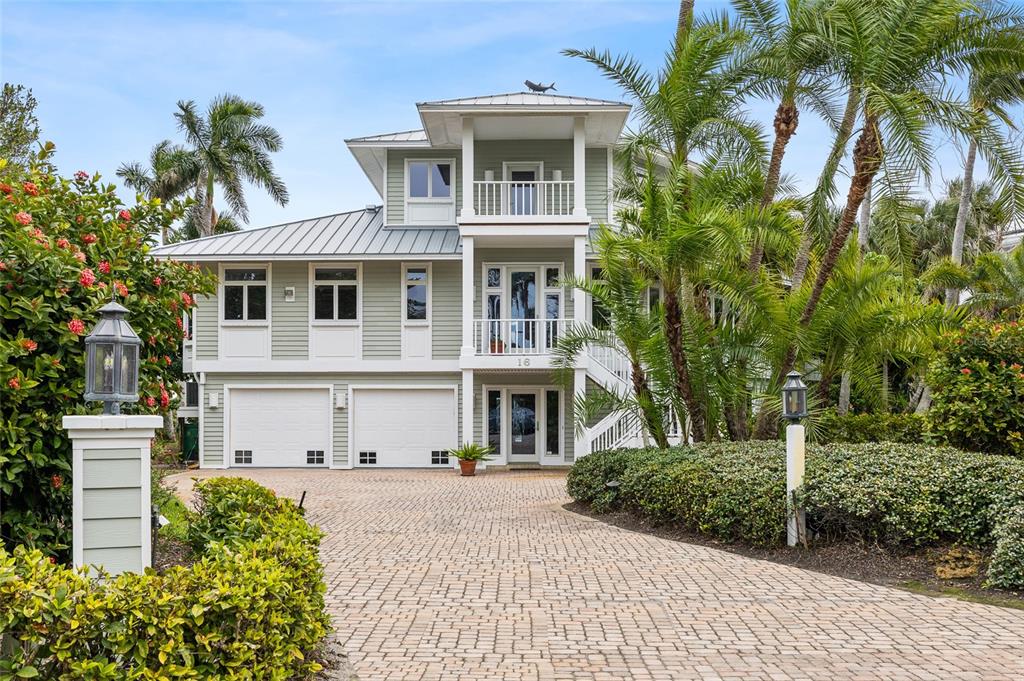 A three-story light green house with a paved driveway and palm trees in the front — 16 GROUPER HOLE DRIVE, BOCA GRANDE, FL