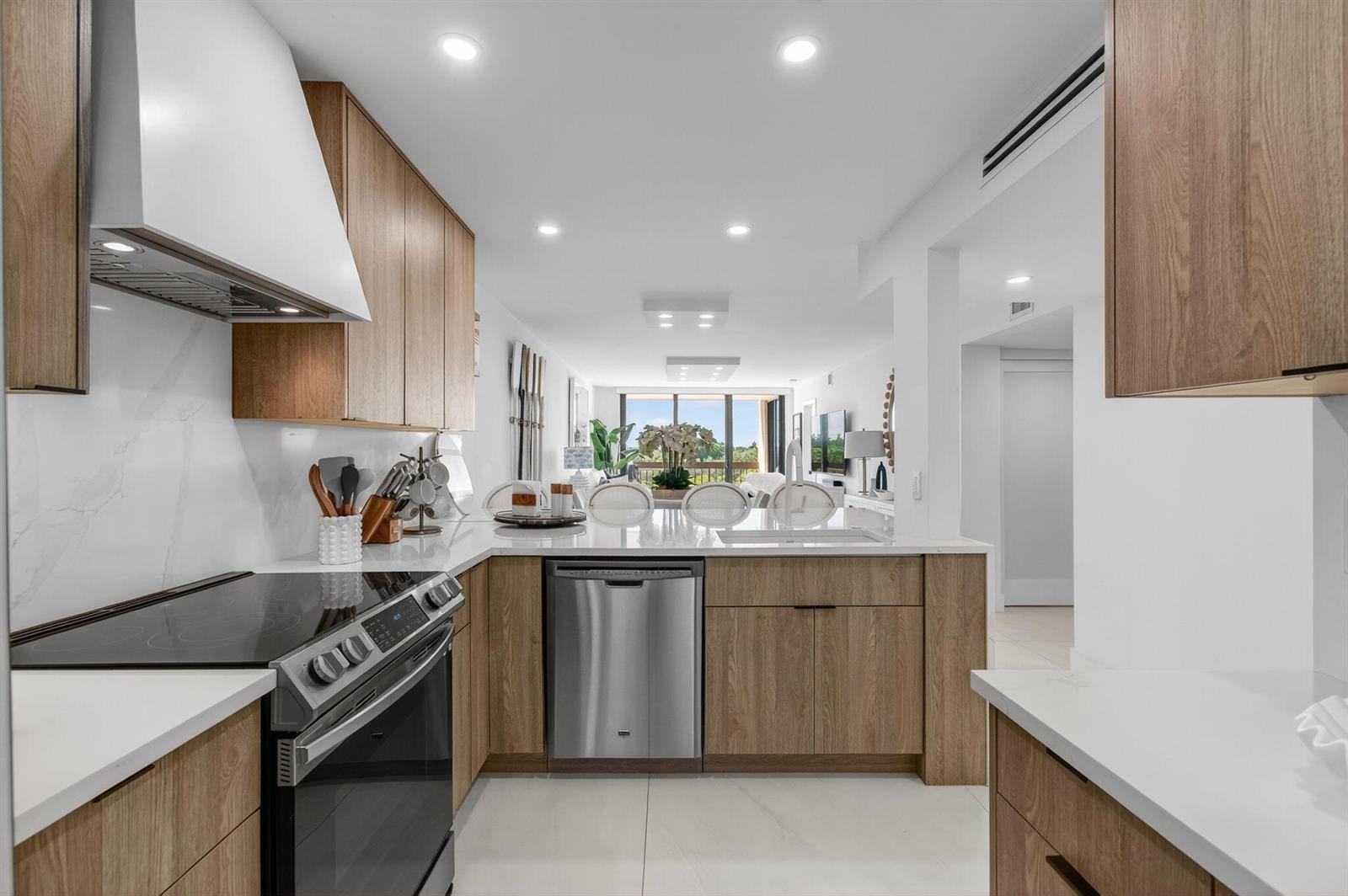 A modern kitchen features light wood cabinets, white countertops, stainless steel appliances, and tile flooring — 600 Egret Circle # 7501, Delray Beach FL 33444, DELRAY BEACH, FL