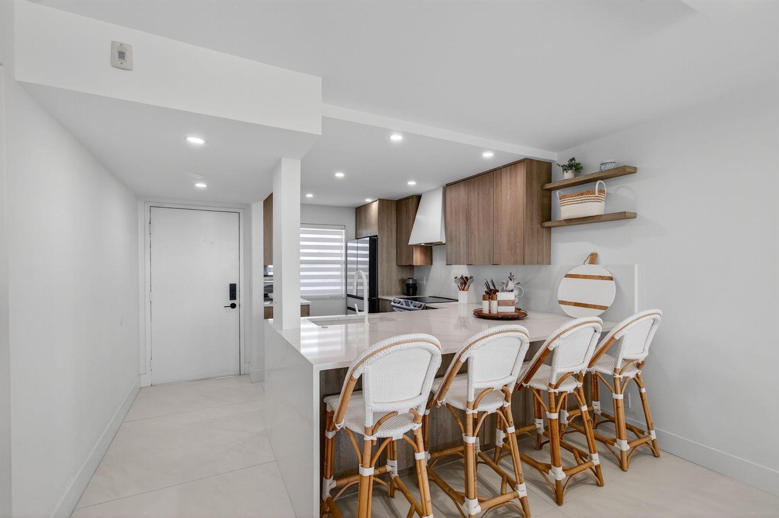 A modern kitchen features a white quartz island with four rattan bar stools — 600 Egret Circle # 7501, Delray Beach FL 33444, DELRAY BEACH, FL