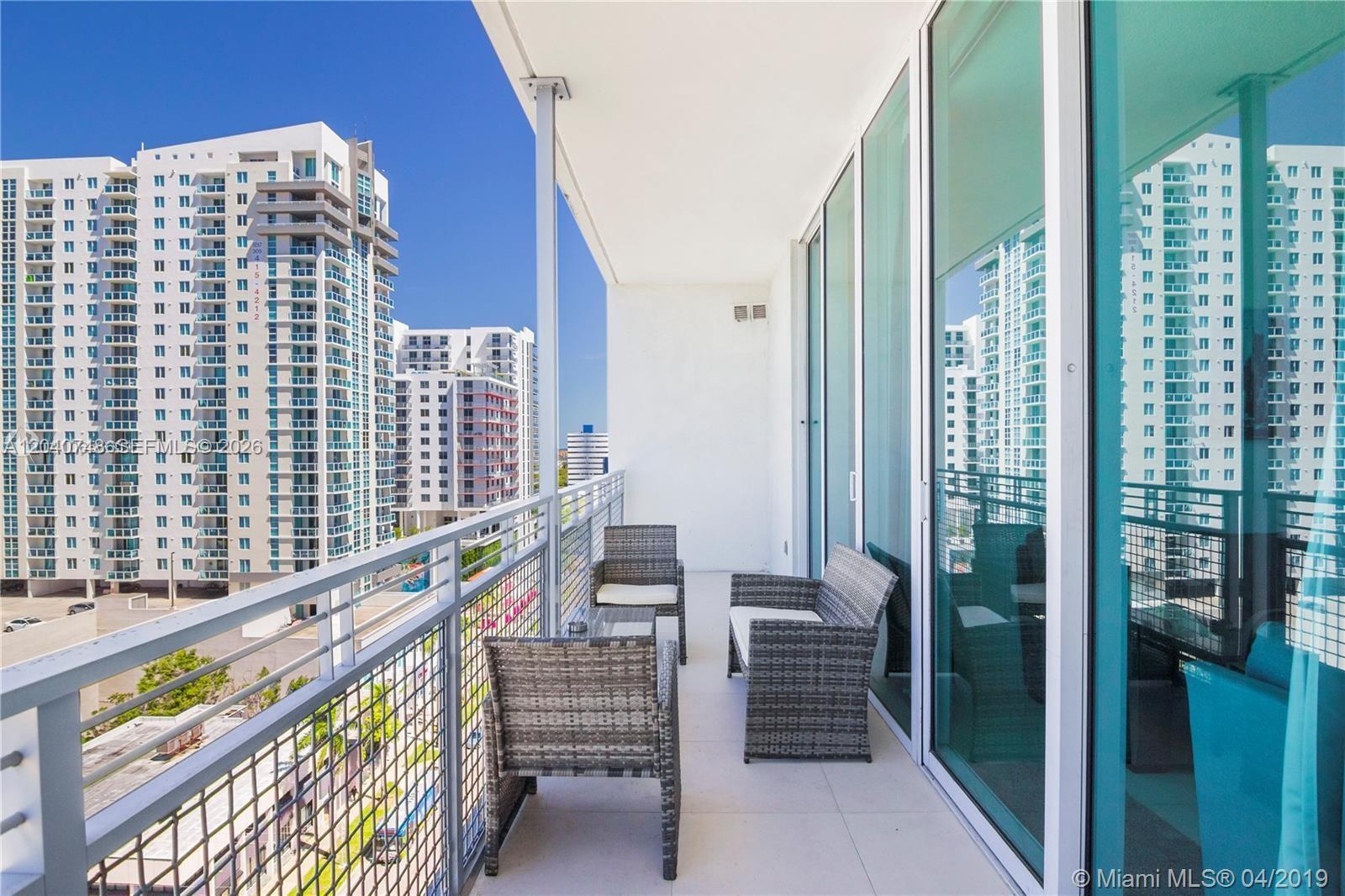 A balcony with wicker furniture overlooks a city street and tall residential buildings — 350 NE 24th St # 1109, Miami FL 33137, MIAMI, FL