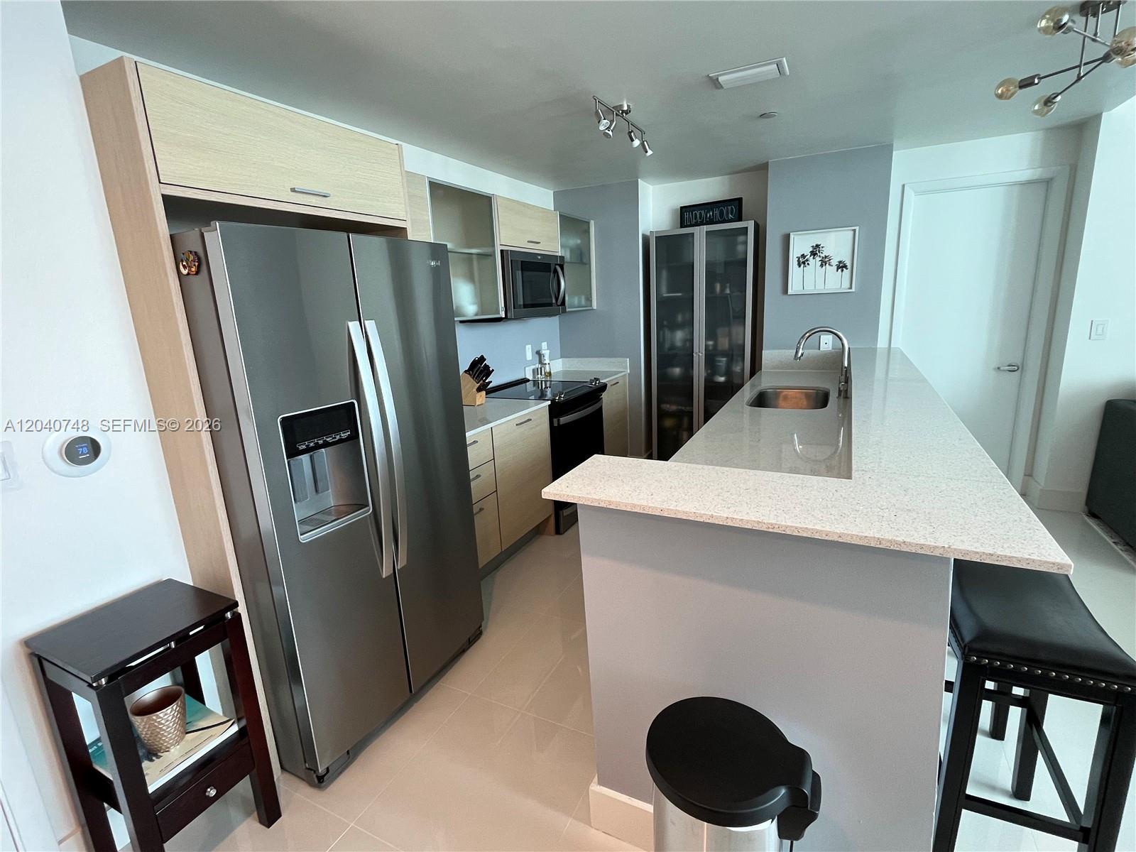 A modern kitchen features stainless steel appliances, light wood cabinetry, and a quartz breakfast bar — 350 NE 24th St # 1109, Miami FL 33137, MIAMI, FL
