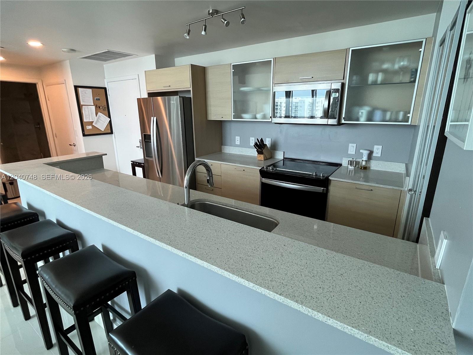 A kitchen features light wood cabinets, stainless steel appliances, and a gray quartz breakfast bar — 350 NE 24th St # 1109, Miami FL 33137, MIAMI, FL