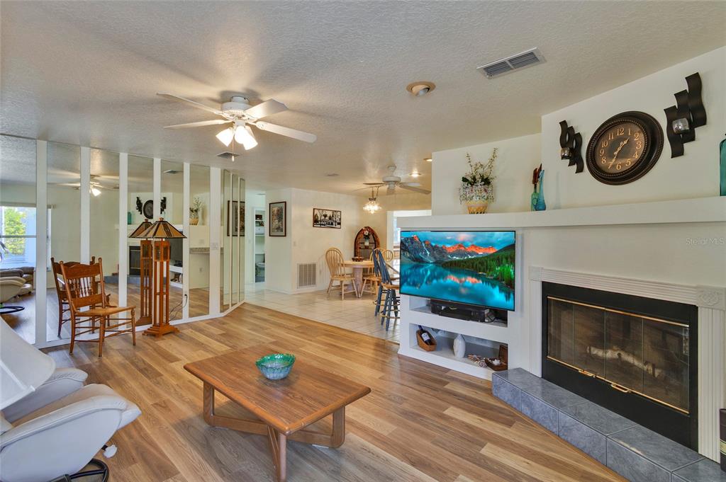 A living room features wood-look flooring, a fireplace with a television, and a mirrored wall — 7095 BLACKBIRD AVENUE, WEEKI WACHEE, FL