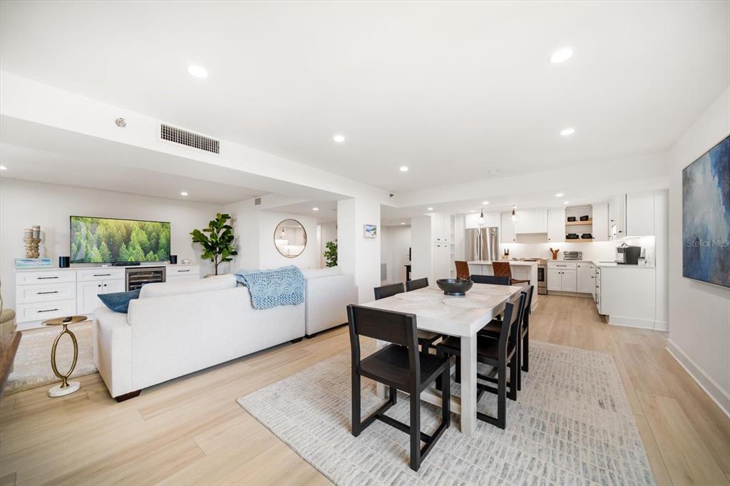 An open-concept living and dining area features white cabinetry, light wood flooring, and modern furniture — 1480 GULF BOULEVARD UNIT 401, CLEARWATER BEACH, FL