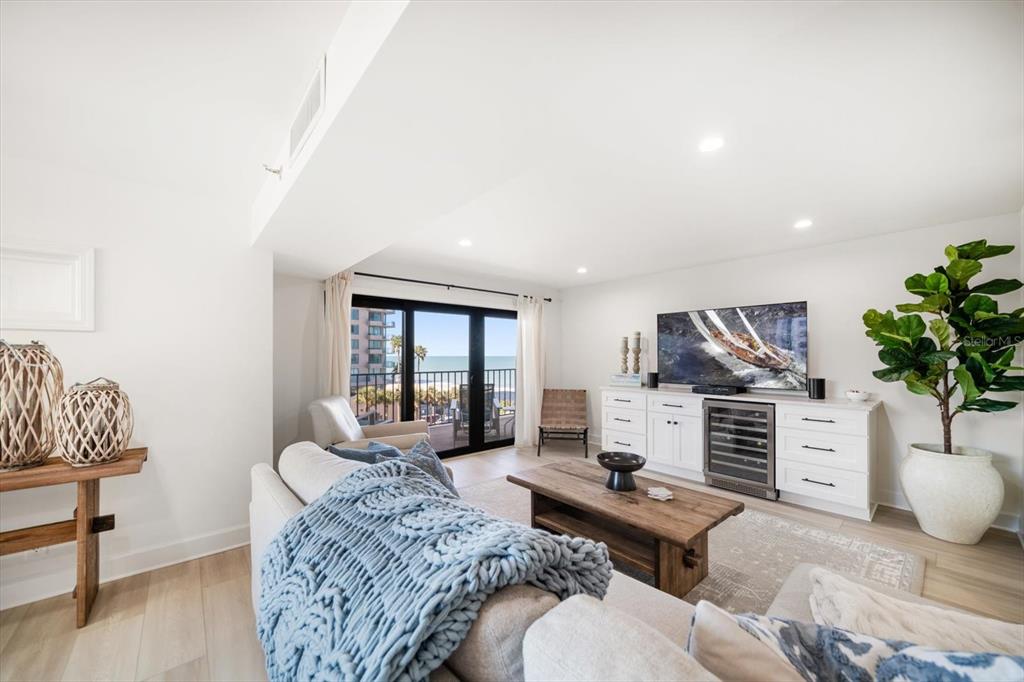 A bright living room features a white media console, a wooden coffee table, and balcony views — 1480 GULF BOULEVARD UNIT 401, CLEARWATER BEACH, FL