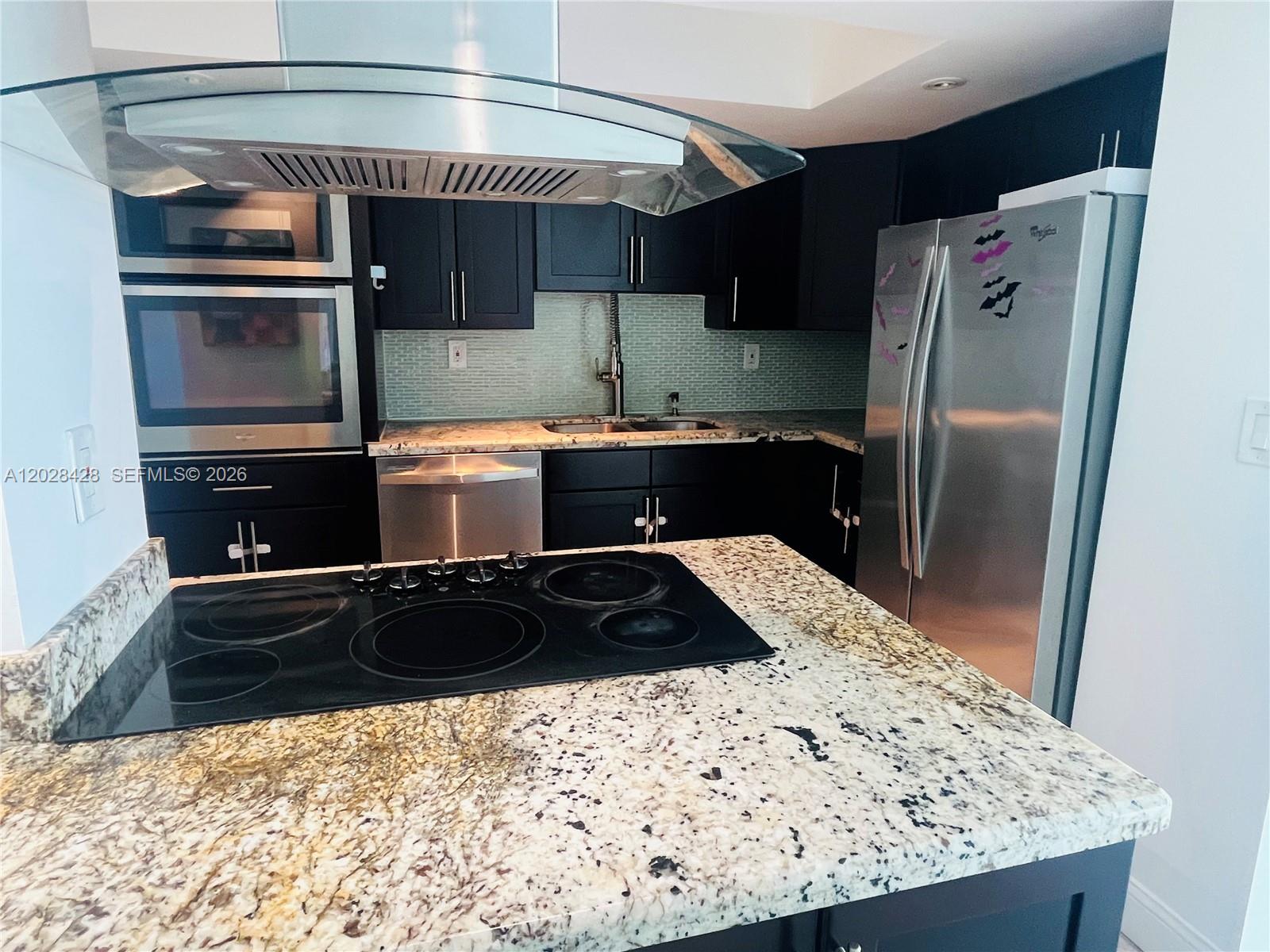 A kitchen features dark cabinetry, granite countertops, stainless steel appliances, and a glass range hood — 2655 Collins Ave # 602, Miami Beach FL 33140, MIAMI BEACH, FL