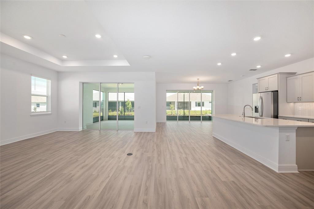 An open-concept living area with light wood-look flooring, a kitchen island, and sliding glass doors — 10187 SW 84TH LANE, OCALA, FL