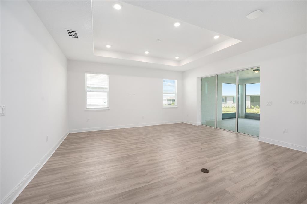 A bright, empty living room features light wood-look flooring, a tray ceiling, and sliding doors — 10187 SW 84TH LANE, OCALA, FL