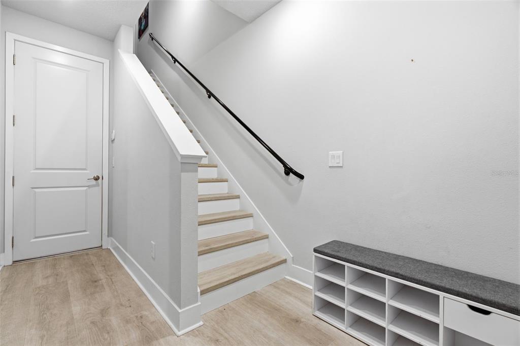 A staircase with light wood treads and a black handrail sits beside a shoe bench — 2511 N GRADY AVENUE UNIT 23, TAMPA, FL