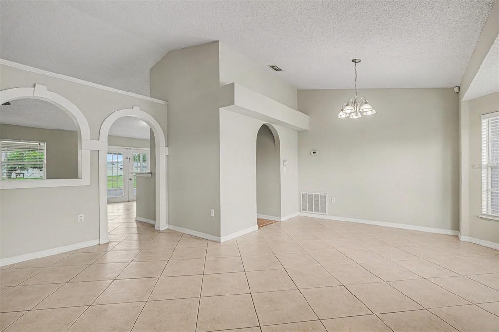 An open dining area with beige tile floors, arched doorways, and a hanging light fixture — 821 JARNAC DRIVE, KISSIMMEE, FL