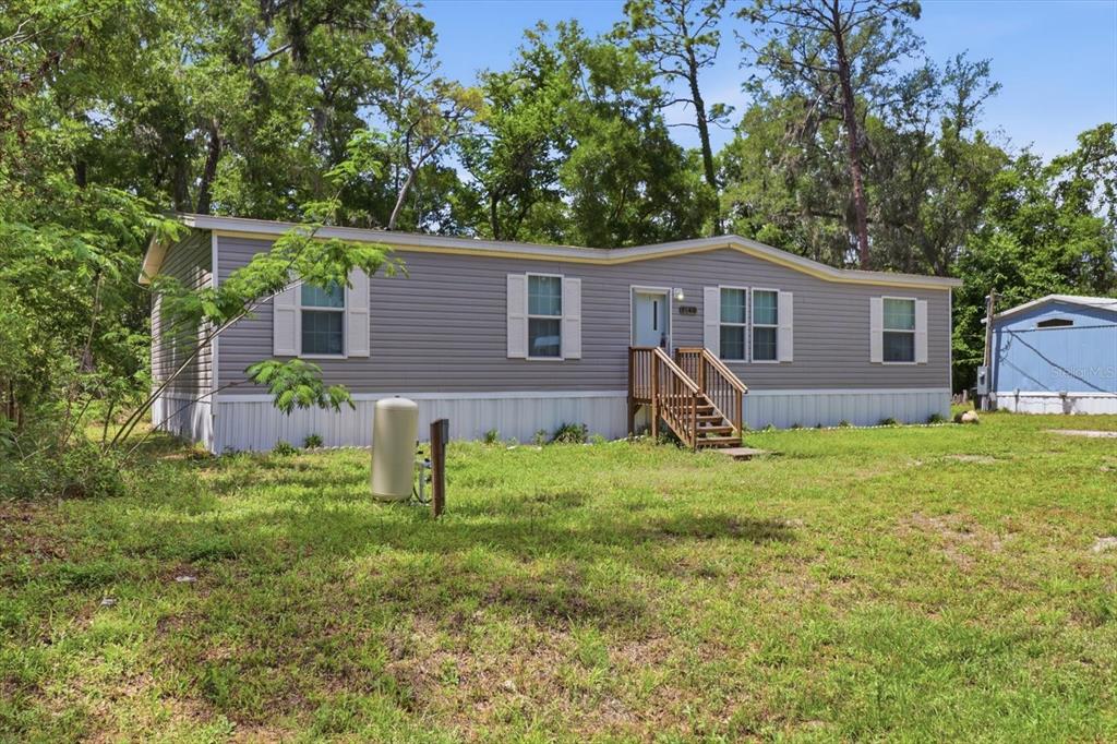 A single-story manufactured home with grey siding sits on a grassy lot with trees — 1140 NW 110TH COURT, OCALA, FL