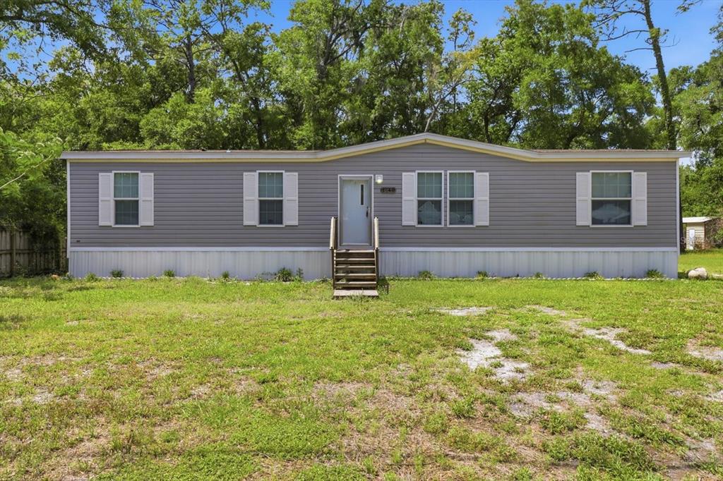 A single-story manufactured home with gray siding and white shutters sits on a grassy lot — 1140 NW 110TH COURT, OCALA, FL