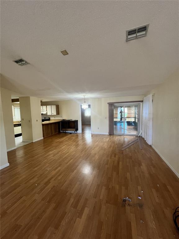 A spacious living room with wood-look flooring leads to a kitchen and a sliding glass door — 2 SENECA PATH, PALM COAST, FL