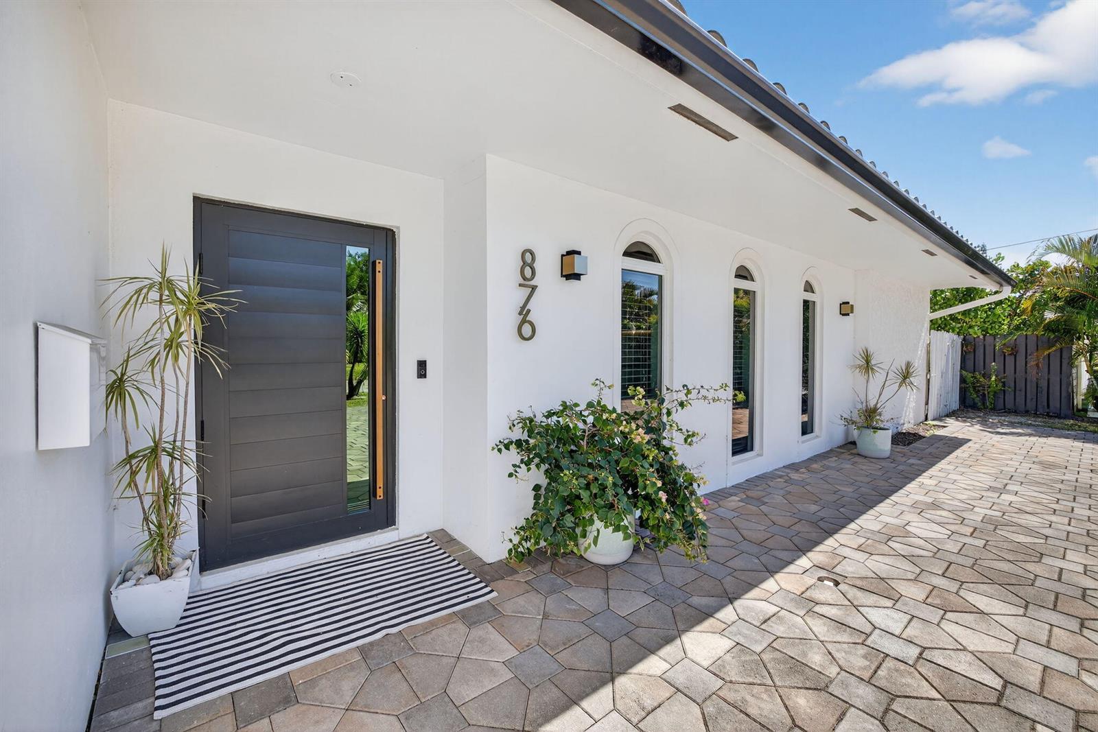 A modern white house exterior features a dark front door, arched windows, and stone pavers — 876 NW 6th Avenue, Boca Raton FL 33432, BOCA RATON, FL
