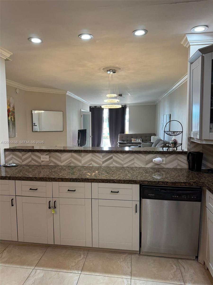 A kitchen with white cabinets, granite countertops, and a chevron backsplash overlooks a living room — 3725 S Ocean Dr # L12, Hollywood FL 33019, HOLLYWOOD, FL