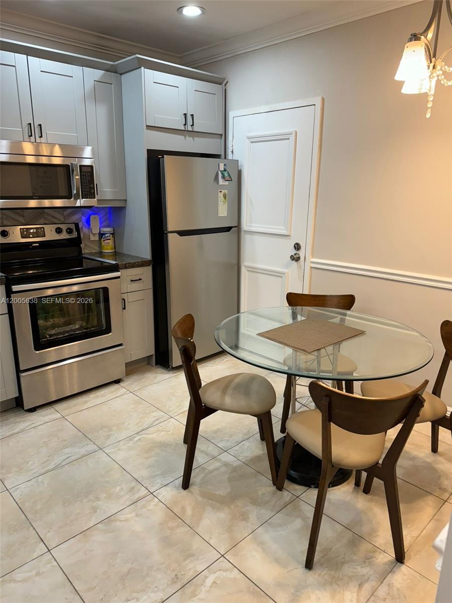 A kitchen features light gray cabinets, stainless steel appliances, and a glass-topped dining table — 3725 S Ocean Dr # L12, Hollywood FL 33019, HOLLYWOOD, FL