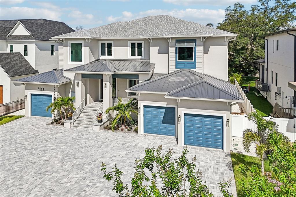 An exterior view of a two-story house with a paved driveway and blue garage doors — 3013 S WEST SHORE BOULEVARD, TAMPA, FL