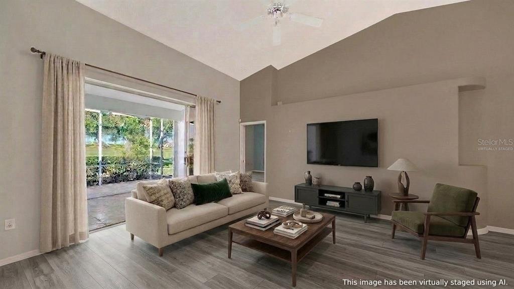 This is a virtually staged living room with vaulted ceilings, gray flooring, and sliding glass doors — 8928 WHITEMARSH AVENUE, SARASOTA, FL