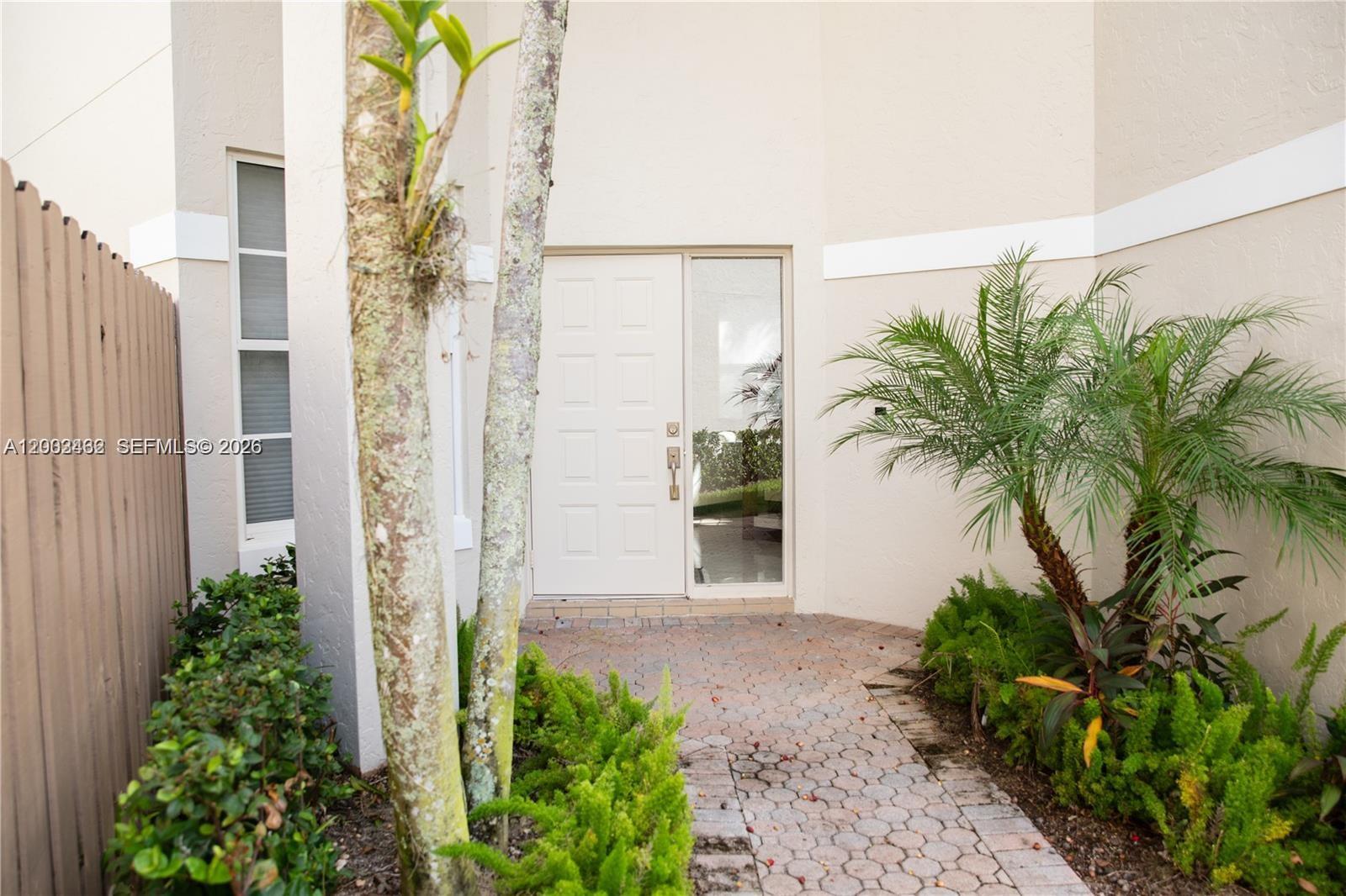 A paved walkway leads to a white front door with a side window and landscaping — 2485 NW 66th Dr # 0, Boca Raton FL 33496, BOCA RATON, FL