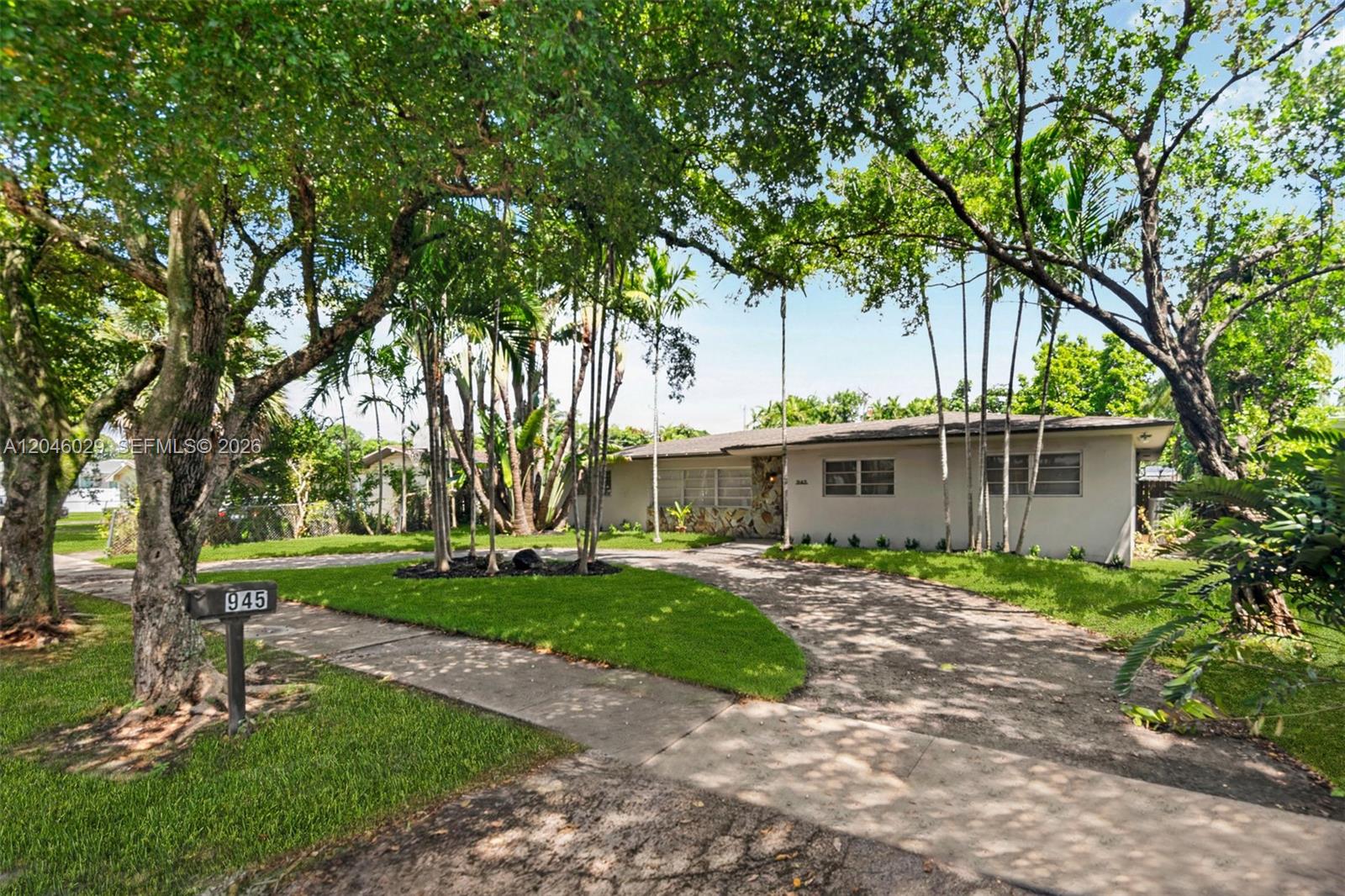 A single-story house with a stone facade and a curved driveway sits among mature trees — 945 NE 176th St, Miami FL 33162, MIAMI, FL