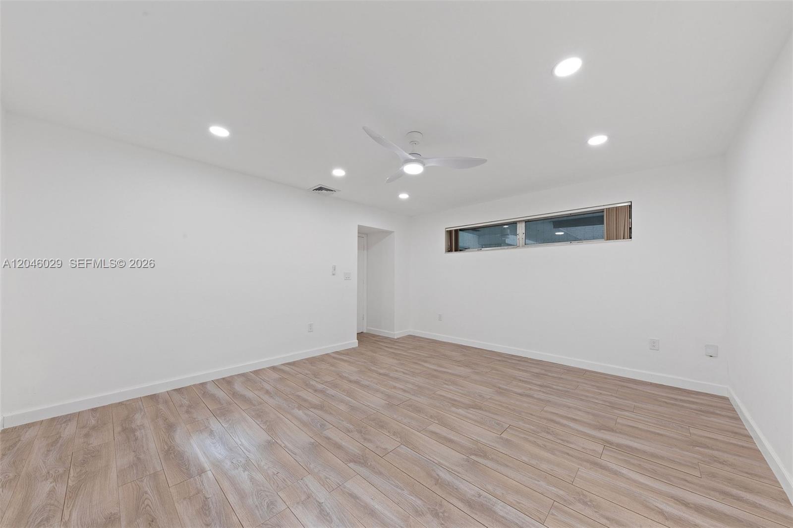 A minimalist room features white walls, light wood-look flooring, recessed lighting, and a ceiling fan — 945 NE 176th St, Miami FL 33162, MIAMI, FL