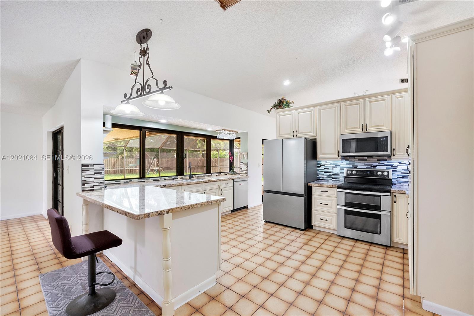 A kitchen features a granite-topped island, stainless steel appliances, and light-colored cabinetry — 11111 NW 7th St, Coral Springs FL 33071, CORAL SPRINGS, FL