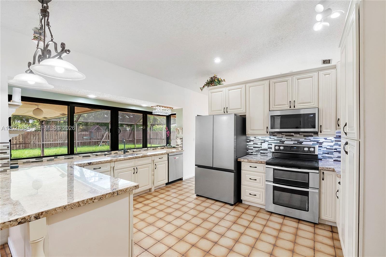 A kitchen features off-white cabinets, stainless steel appliances, granite countertops, and tiled flooring — 11111 NW 7th St, Coral Springs FL 33071, CORAL SPRINGS, FL