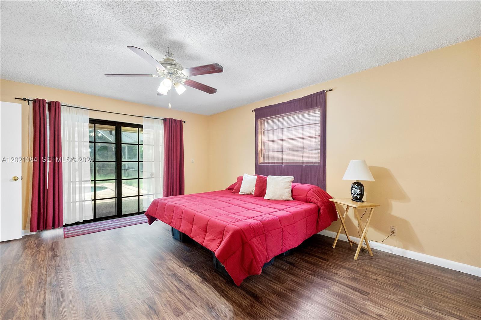 A bedroom features a red bed, wood-look flooring, sliding glass doors, and a ceiling fan — 11111 NW 7th St, Coral Springs FL 33071, CORAL SPRINGS, FL