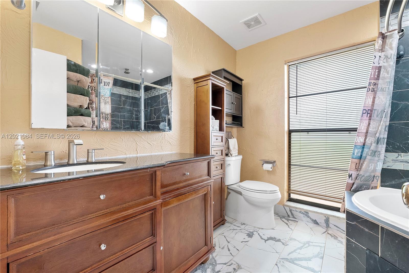 A bathroom features a wooden vanity, marble-look tile flooring, and a shower with dark tiles — 11111 NW 7th St, Coral Springs FL 33071, CORAL SPRINGS, FL